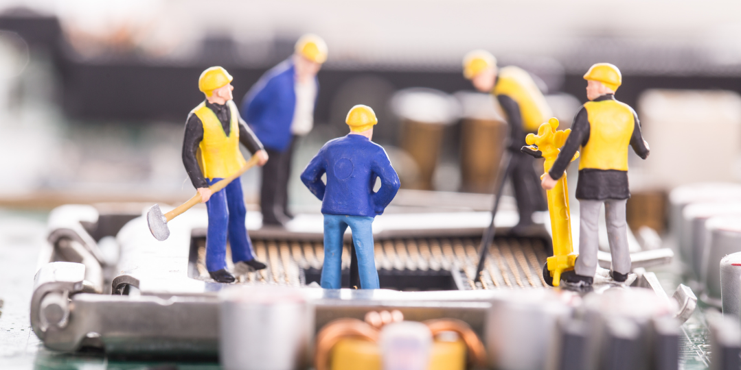 Miniature construction workers standing on a computer motherboard, symbolizing technical maintenance and repair.