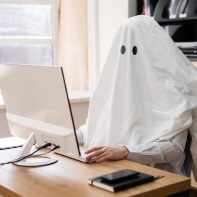 Person dressed as a ghost sitting at a desk using a computer, symbolizing what to do when your web designer ghosts you.